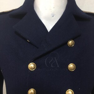 Peut inclure: Un manteau bleu marine &agrave; double boutonnage avec des boutons dor&eacute;s. Le manteau a un design classique avec un col crant&eacute; et une garniture dor&eacute;e sur les &eacute;paules. Les boutons sont grands et ronds, ajoutant une touche d'&eacute;l&eacute;gance.