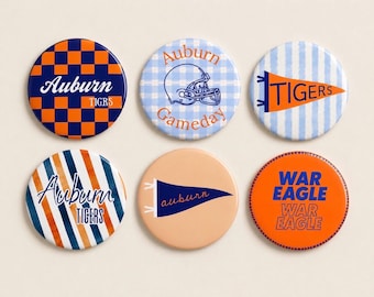 May include: A collection of six round Auburn University-themed buttons. The buttons feature various designs, including checkered patterns, stripes, and pennants, in the team's colors of blue and orange. Text includes "Auburn", "Tigers", "Gameday", and "War Eagle".