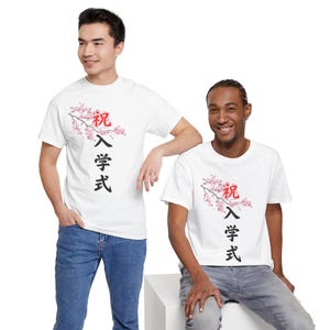 May include: Two people wearing white t-shirts with a Japanese cherry blossom design. The shirts feature a branch with pink flowers and Japanese characters in red and black. The models are wearing blue jeans.