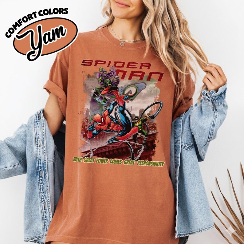 Op de afbeelding: Een roestkleurig t-shirt met een Spider-Man-afbeelding, de tekst "SPIDER-MAN" en de zin "WITH GREAT POWER COMES GREAT RESPONSIBILITY." Het shirt heeft ook de tekst "COMFORT COLORS" en "Yam" in een logo.
