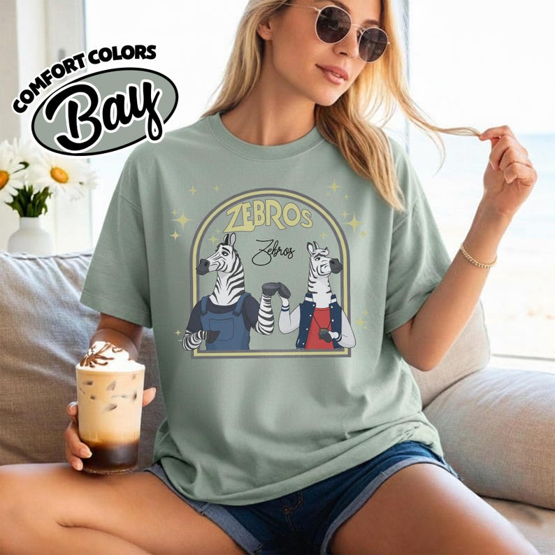May include: A pale green t-shirt featuring a graphic of two zebras shaking hands, with the text "ZEBROS" above and "Zebros" below. The shirt also has the text "COMFORT COLORS Bay" in a circular design.