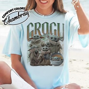 K&ouml;nnte beinhalten: Ein hellblaues T-Shirt mit dem Text COMFORT COLORS Chambray und GROGU in einer stilisierten Schriftart. Die Grafik zeigt f&uuml;nf Illustrationen der Figur Grogu in verschiedenen Posen, darunter eine in einer runden, schwebenden Kapsel.