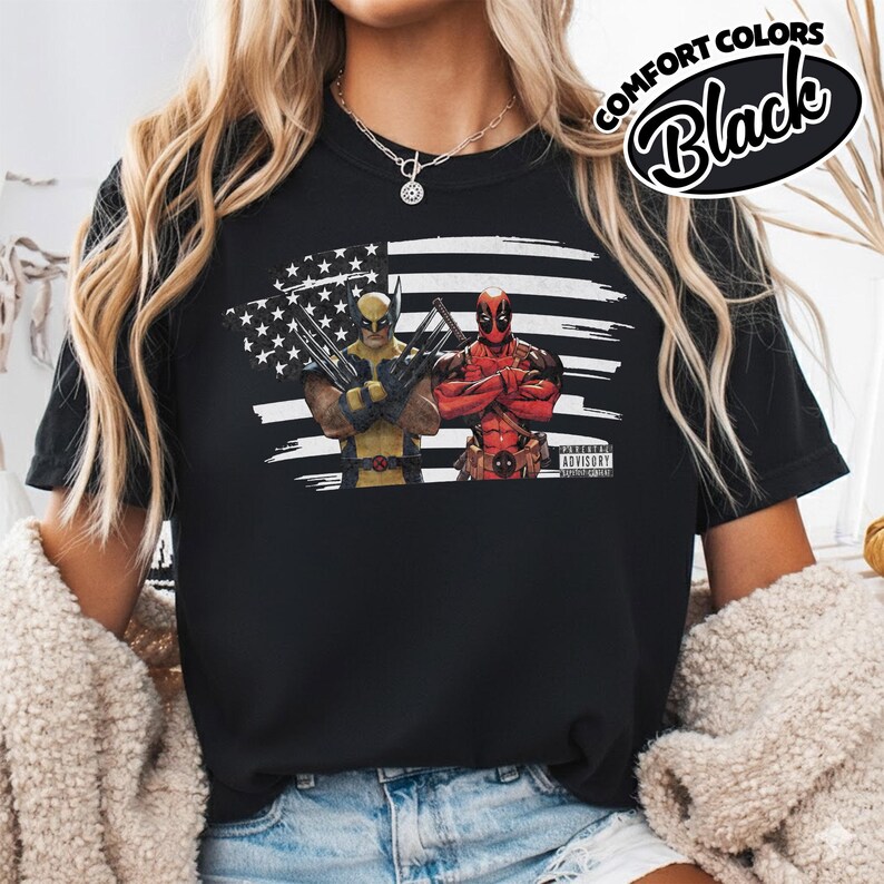 May include: A black t-shirt featuring a graphic print of Wolverine and Deadpool standing in front of a stylized American flag. The design includes a small Parental Advisory label in the corner and the text Comfort Colors Black in the upper right.