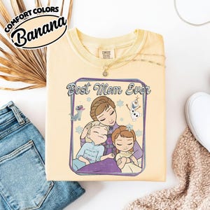 May include: A light yellow Comfort Colors t-shirt with the text "Best Mom Ever" and a graphic of a mother and two children. The shirt also features the text "Comfort Colors" and the word "Banana".