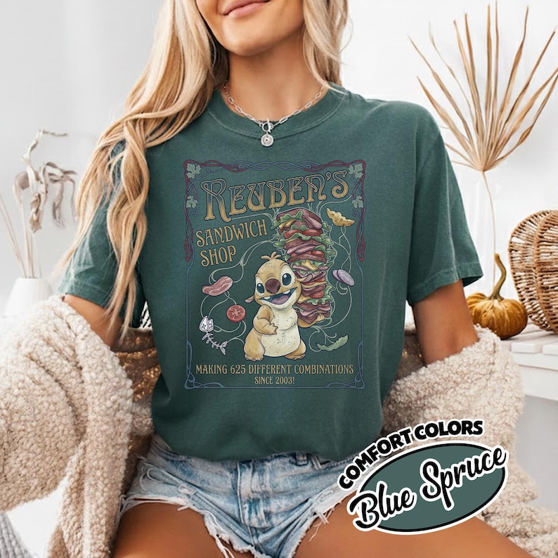 K&ouml;nnte beinhalten: Blau-Fichte Comfort Colors T-Shirt mit einem Reuben's Sandwich Shop-Motiv. Das Design zeigt eine Zeichentrickfigur, ein gro&szlig;es Sandwich und den Text "MAKING 625 DIFFERENT COMBINATIONS SINCE 2003".