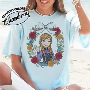 Peut inclure: T-shirt bleu clair avec un dessin d'un personnage de dessin anim&eacute; dans une couronne florale. Le personnage fait un clin d'&oelig;il et fait signe de la main. Le t-shirt porte les mots "COMFORT COLORS" et "Chambray".