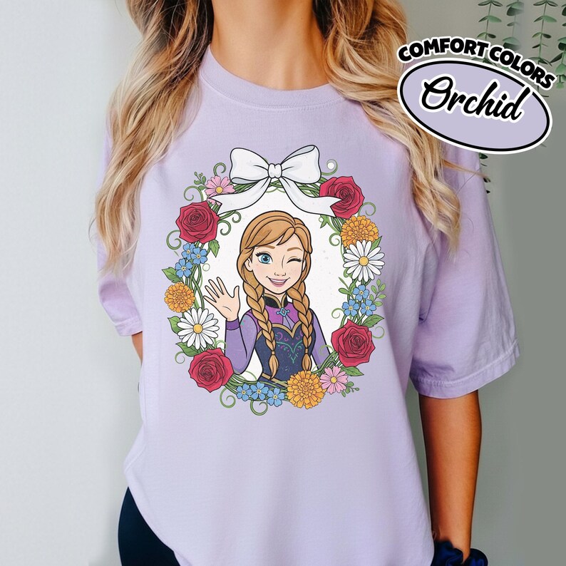 Peut inclure: T-shirt lilas clair avec un dessin d'un personnage de dessin anim&eacute; dans une couronne florale. Le personnage fait un clin d'&oelig;il et fait signe de la main. Le t-shirt porte les mots "COMFORT COLORS" et "Orchid".