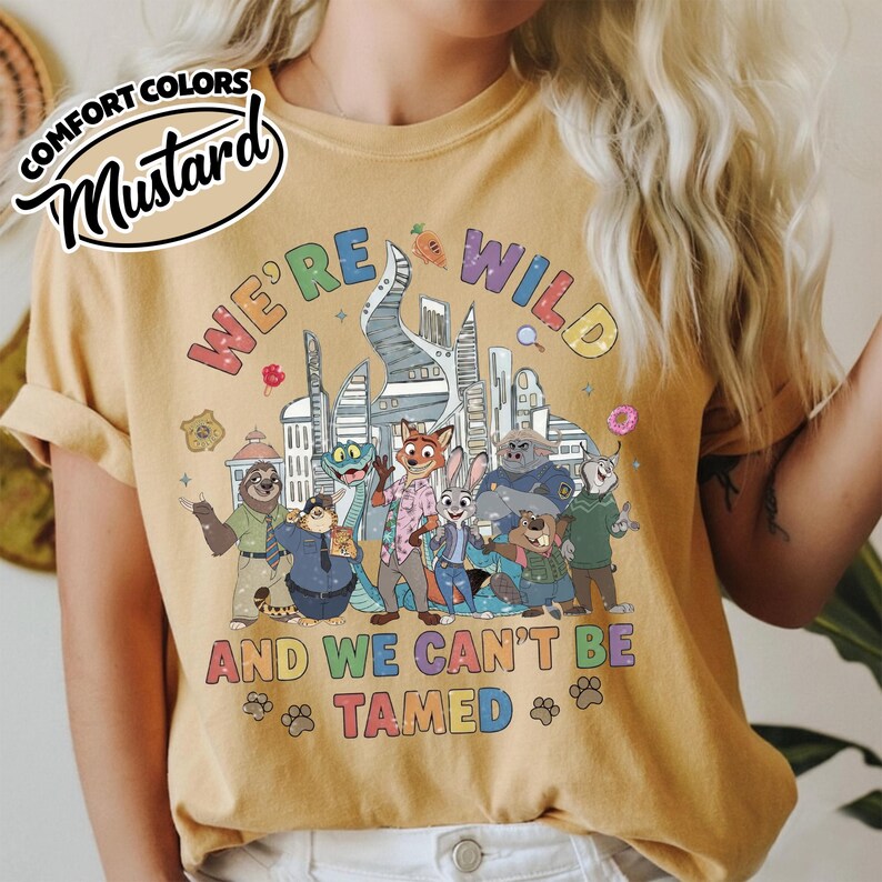 May include: Mustard-colored t-shirt with the text "WE'RE WILD AND WE CAN'T BE TAMED" and a graphic of cartoon animals in front of a city skyline. The shirt has a Comfort Colors label.