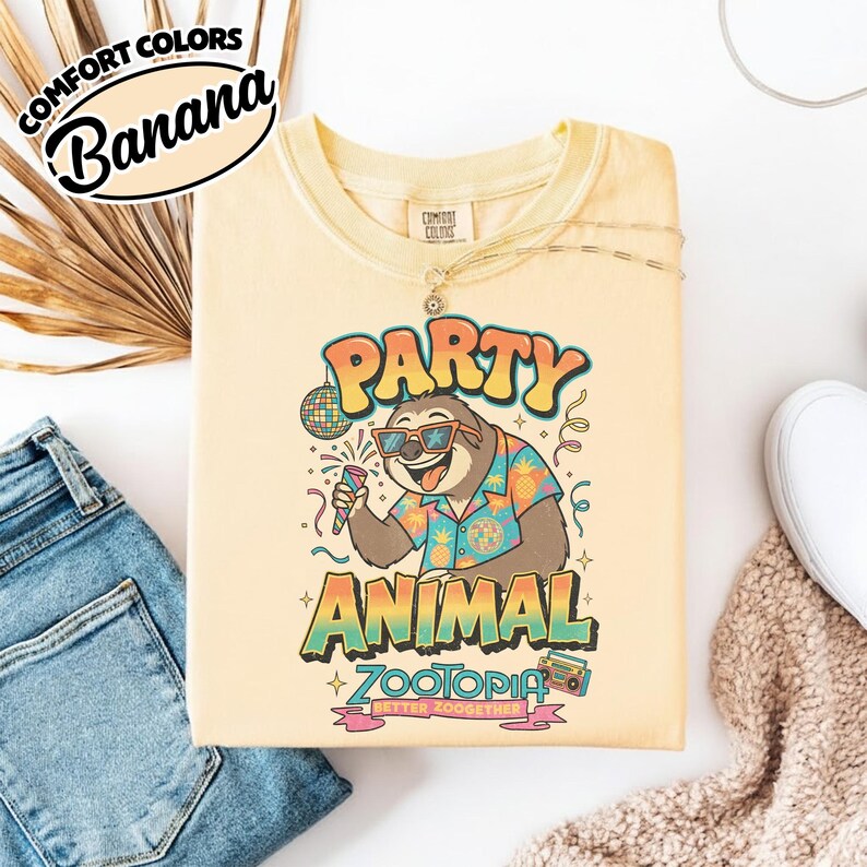 Puede incluir: Una camiseta Comfort Colors amarillo claro con un gr&aacute;fico de un perezoso con gafas de sol y una camisa hawaiana, sosteniendo un micr&oacute;fono. El texto dice "PARTY ANIMAL ZOOTOPIA". La camiseta se muestra con vaqueros azules y zapatillas blancas.
