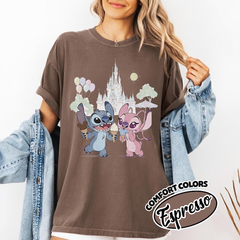 Puede incluir: Camiseta color espresso con un gr&aacute;fico de Stitch y Angel sosteniendo conos de helado frente a un castillo. El dise&ntilde;o incluye globos, &aacute;rboles y un sol. La camiseta tiene las palabras "COMFORT COLORS" y "Espresso" en un dise&ntilde;o circular.