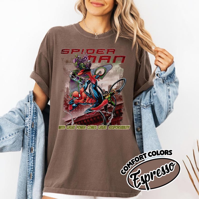 Op de afbeelding: Espresso-kleurig T-shirt met een Spider-Man-afbeelding. Het ontwerp toont Spider-Man in actie met schurken, de tekst "SPIDER-MAN" en de zin "WITH GREAT POWER COMES GREAT RESPONSIBILITY". Het shirt heeft een vintage uitstraling.