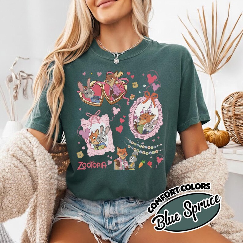 May include: A dark green short-sleeve t-shirt featuring a Zootopia graphic print. The design includes illustrations of Judy Hopps and Nick Wilde inside ornate frames, surrounded by small hearts, balloons, and the text Zootopia in pink.