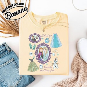 Op de afbeelding: Een lichtgeel sweatshirt met een grafisch ontwerp met personages en elementen uit de film Frozen. Het ontwerp bevat de tekst "Let it go" en "Worth melting for..." samen met afbeeldingen van Anna, Elsa, Olaf en andere personages.
