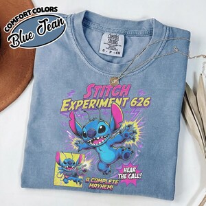Może przedstawiać: Niebieska koszulka z kr&oacute;tkim rękawem z grafiką przedstawiającą postać Stitcha z Lilo i Stitch. Nadruk zawiera tekst "STITCH EXPERIMENT 626", "HEAR THE CALL!" oraz "A COMPLETE MAYHEM!" z błyskawicami i panelem w stylu komiksowym.