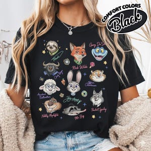 K&ouml;nnte beinhalten: Schwarzes T-Shirt mit Cartoon-Charakterportr&auml;ts aus Zootopia, darunter Flash, Nick Wilde und Judy Hopps. Das Shirt tr&auml;gt die Aufschrift "COMFORT COLORS" und "Black". Das Design enth&auml;lt Charakternamen und andere Details.