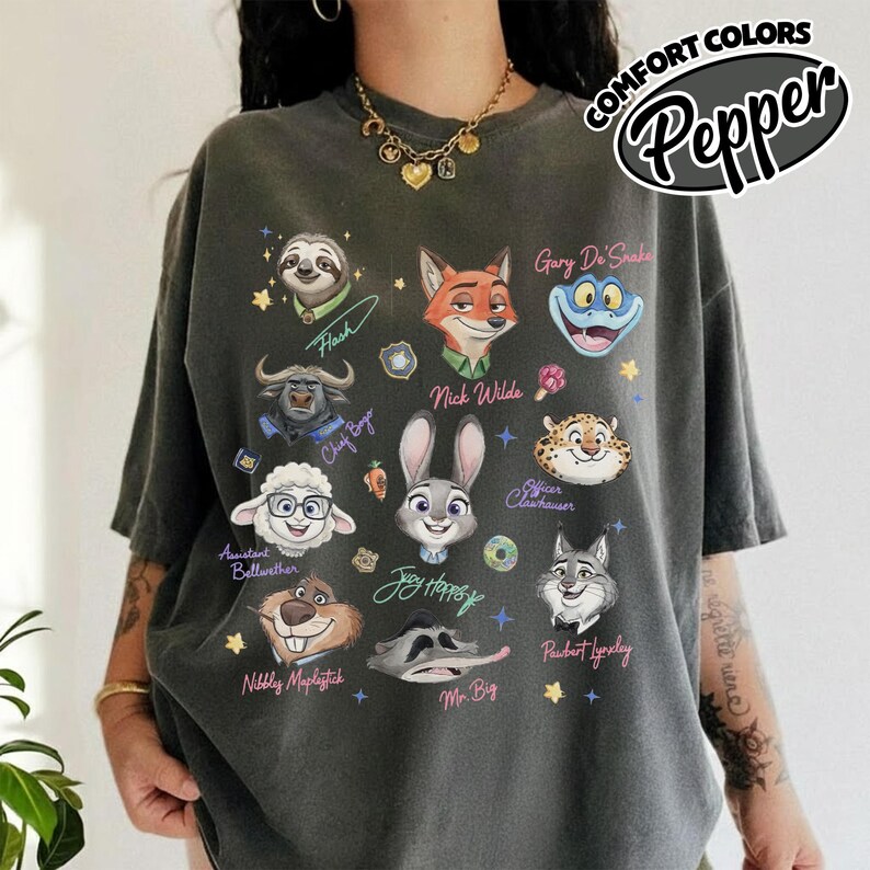 K&ouml;nnte beinhalten: Dunkelgraues T-Shirt mit Cartoon-Charakterportr&auml;ts, darunter Nick Wilde und Judy Hopps. Das Shirt tr&auml;gt die Aufschrift "COMFORT COLORS" und "Pepper". Das T-Shirt hat eine lockere Passform.
