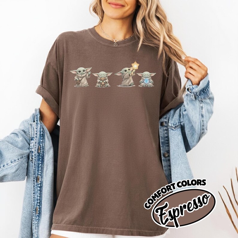 以下が含まれることがあります： 4つのグログのイラストが特徴の、エスプレッソカラーのTシャツ。グラフィックは、星と宝石を持っている様々なポーズのグログを描いています。シャツは袖をまくり上げており、「COMFORT COLORS Espresso」の文字が円形にデザインされています。