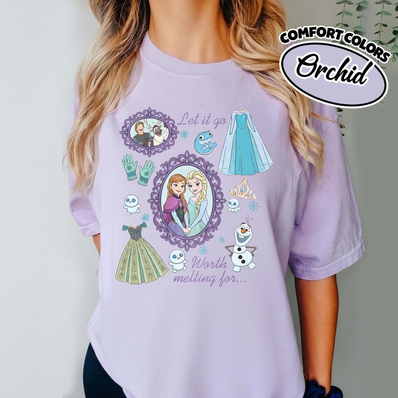 Op de afbeelding: Een lichtpaars T-shirt met een grafisch ontwerp met personages en elementen uit een populaire animatiefilm. Het ontwerp bevat ingelijste portretten, jurken, sneeuwvlokken en de tekst "Let it go" en "Worth melting for...". Het shirt is gelabeld met "Comfort Colors" en "Orchid".