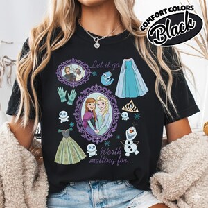 Op de afbeelding: Zwart T-shirt met een afbeelding van personages en elementen uit de film Frozen. Het ontwerp bevat afbeeldingen van Anna en Elsa, Olaf en de tekst "Let it go" en "Worth melting for..."
