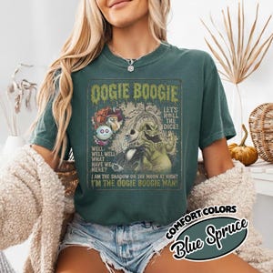 May include: Blue Spruce Comfort Colors t-shirt featuring a graphic of Oogie Boogie with text that reads "Oogie Boogie" and "I'm the Oogie Boogie Man!". The shirt has a vintage, distressed design.