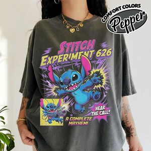Może przedstawiać: Ciemnoszary t-shirt z grafiką przedstawiającą niebieską postać Stitcha z Lilo i Stitch. Napis głosi STITCH EXPERIMENT 626, HEAR THE CALL! oraz A COMPLETE MAYHEM. Wz&oacute;r zawiera fioletowe błyskawice i ż&oacute;łtą ramkę z mniejszą grafiką.