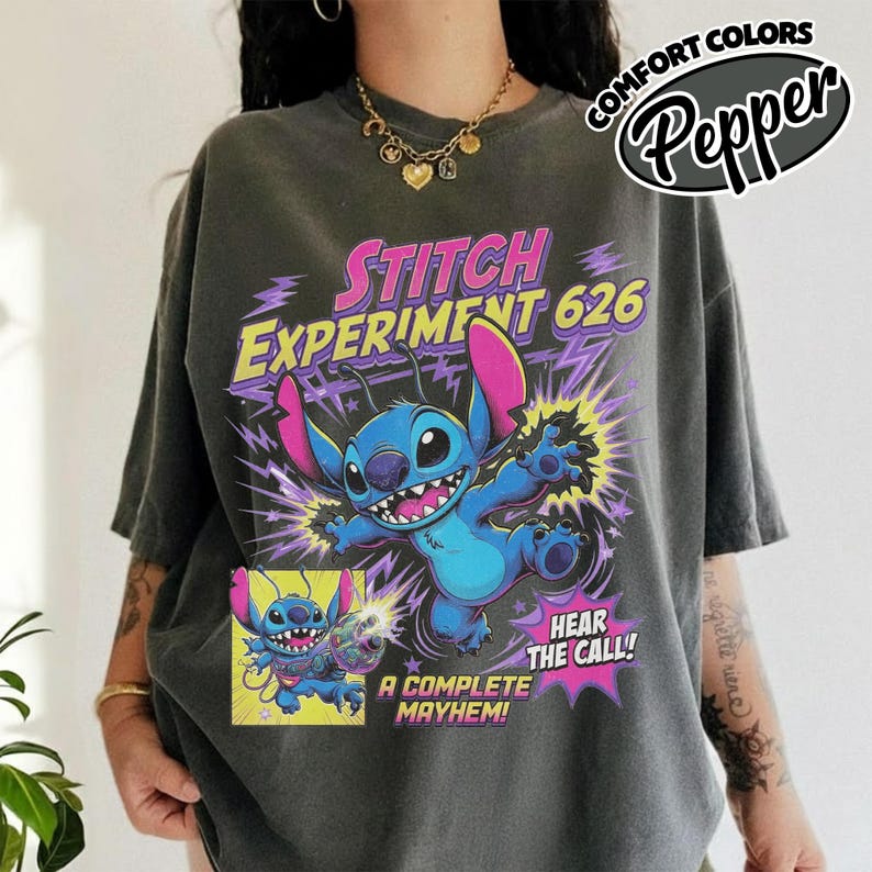 Może przedstawiać: Ciemnoszary t-shirt z grafiką przedstawiającą niebieską postać Stitcha z Lilo i Stitch. Napis głosi STITCH EXPERIMENT 626, HEAR THE CALL! oraz A COMPLETE MAYHEM. Wz&oacute;r zawiera fioletowe błyskawice i ż&oacute;łtą ramkę z mniejszą grafiką.