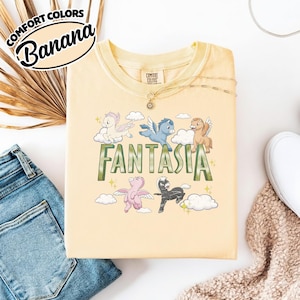 May include: A pale yellow t-shirt with the word "FANTASIA" in green. The shirt features cartoon pegasus characters in various colours, including white, blue, and pink. The shirt has the words "COMFORT COLORS" and "Banana" in a circular design.