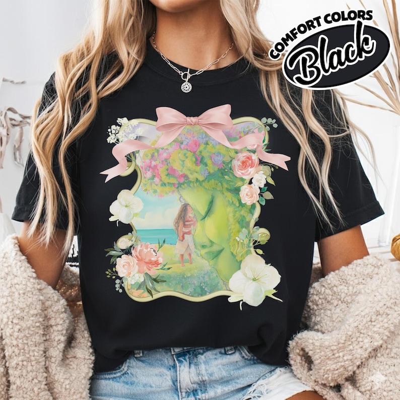 K&ouml;nnte beinhalten: Schwarzes T-Shirt mit einer floralen und Gesichts-Grafik. Die Grafik zeigt ein Frauengesicht mit Blumenkrone, einer rosa Schleife und einem Paar am Strand. Die Worte "COMFORT COLORS Black" sind oben rechts aufgedruckt.