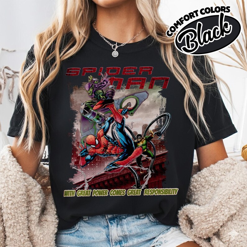Op de afbeelding: Zwart T-shirt met een Spider-Man-afbeelding en de rode tekst "SPIDER-MAN". Het ontwerp toont Spider-Man in actie met andere personages en de zin "WITH GREAT POWER COMES GREAT RESPONSIBILITY". Het shirt heeft "COMFORT COLORS" en "Black" erop gedrukt.