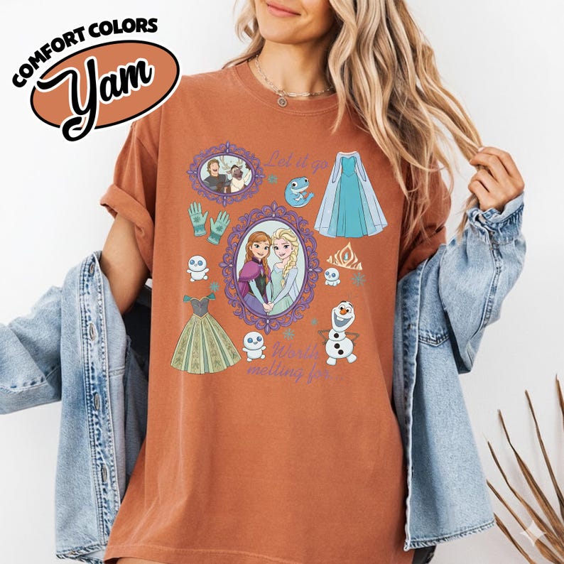 Op de afbeelding: Roestkleurig T-shirt met een grafisch ontwerp met personages en elementen uit de animatiefilm "Frozen". Het ontwerp bevat afbeeldingen van Anna en Elsa, jurken en de tekst "Let it go" en "World melting for you."