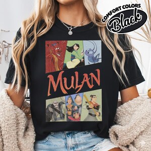 Puede incluir: Camiseta negra con un dise&ntilde;o gr&aacute;fico de personajes de la pel&iacute;cula de animaci&oacute;n Mulan. El dise&ntilde;o incluye im&aacute;genes de Mushu, Mulan y otros personajes, con la palabra "Mulan" en letras naranjas. La camiseta tambi&eacute;n tiene el texto "Comfort Colors Black".