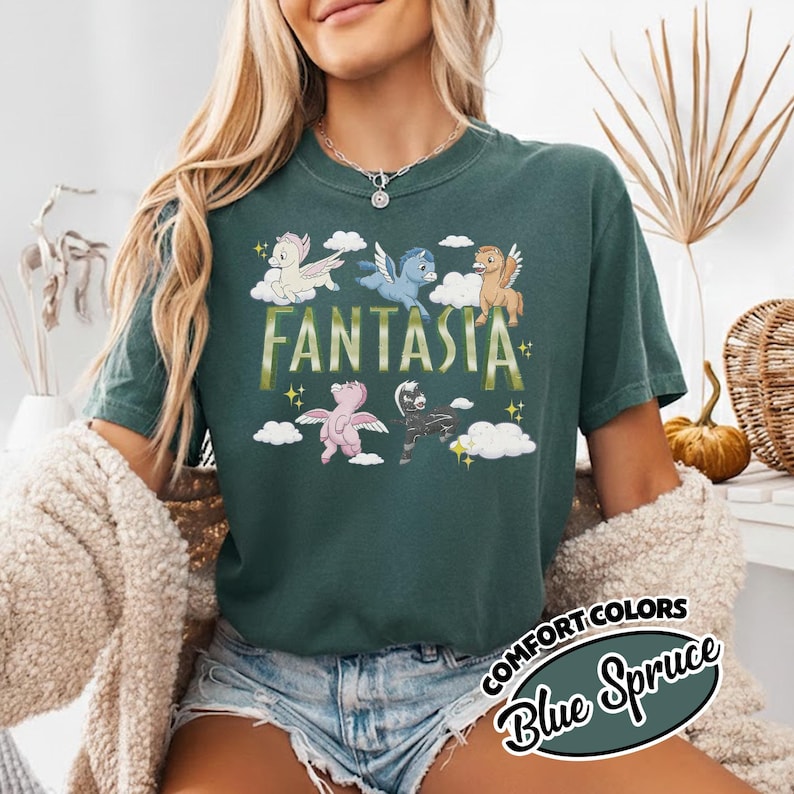 May include: A dark teal t-shirt featuring the word "Fantasia" in gold lettering and cartoon pegasus figures. The shirt also has the words "Comfort Colors" and "Blue Spruce" in a circular design.