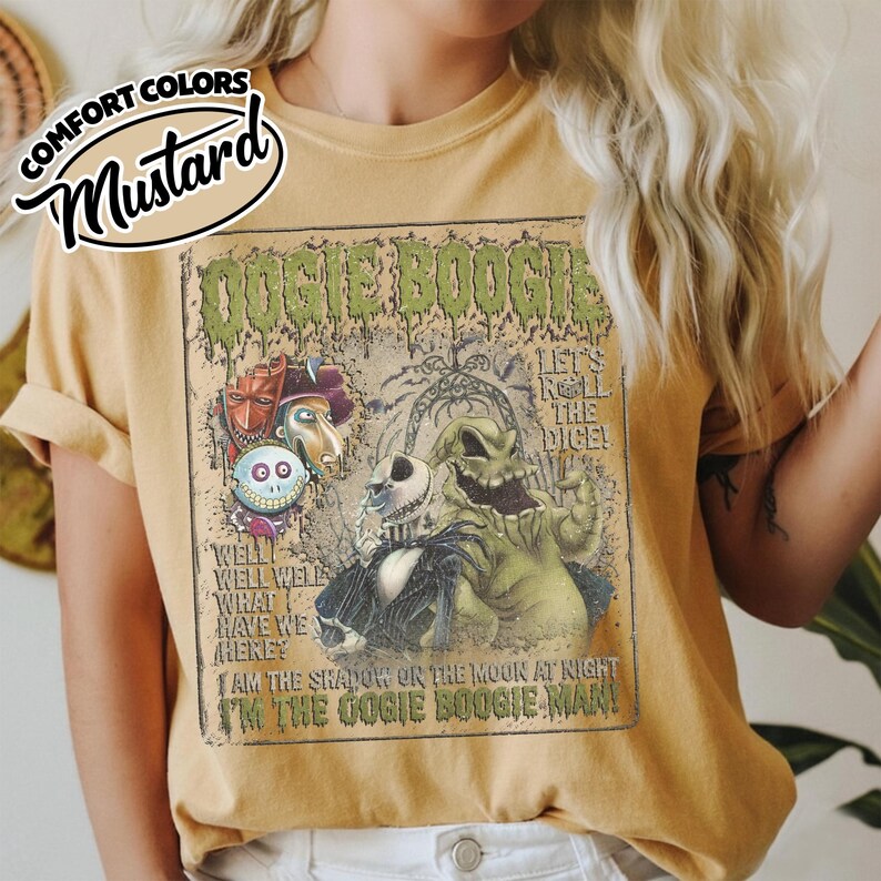 May include: Mustard-colored t-shirt featuring a graphic from "The Nightmare Before Christmas." The design includes characters like Jack Skellington and Oogie Boogie, with text that reads "Oogie Boogie" and "Let's Roll the Dice!"