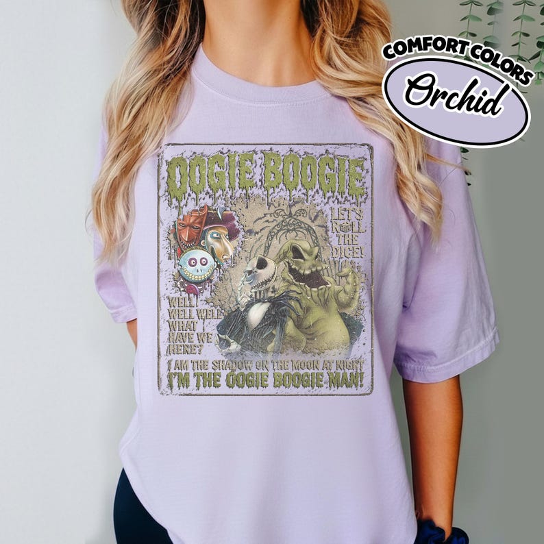 May include: Orchid-colored t-shirt featuring a graphic from "The Nightmare Before Christmas." The design includes the text "Oogie Boogie" and images of characters. The shirt is made of Comfort Colors material.