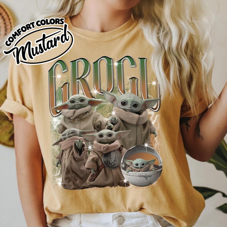 K&ouml;nnte beinhalten: Ein senfgelbes T-Shirt mit einem Grafikdruck des Textes GROGU in gr&uuml;n-braunen Verlaufsbuchstaben. Das Design zeigt vier Illustrationen der Figur Grogu in beigen Roben und einen Grogu in einer silbernen schwebenden Kapsel.