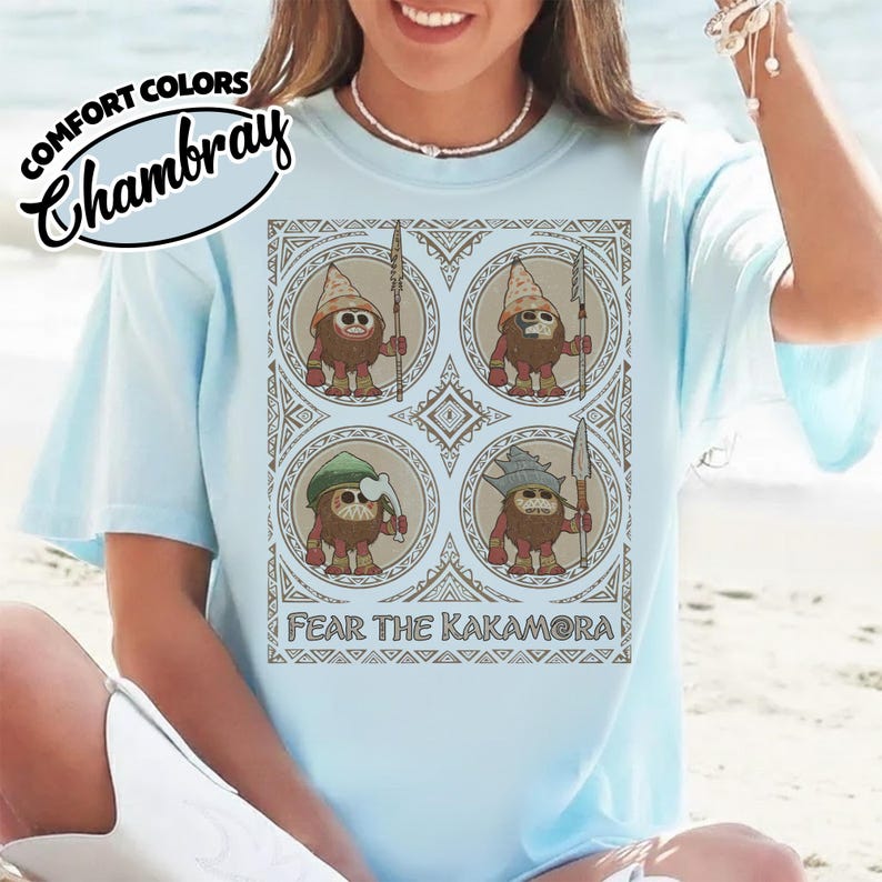 May include: Pale blue t-shirt featuring the text "COMFORT COLORS Chambray" and a graphic of four cartoon figures in circles, each holding a spear. The text "FEAR THE KAKAMORA" is below the graphic.