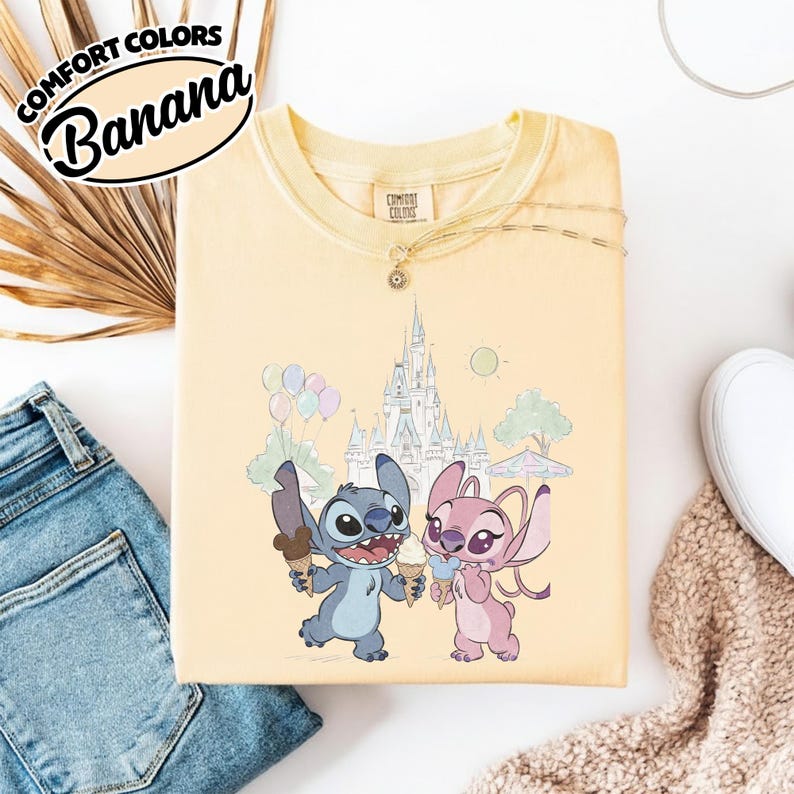 Puede incluir: Camiseta amarilla clara con un gr&aacute;fico de Stitch y Angel sosteniendo conos de helado frente a un castillo. La camiseta tiene las palabras "COMFORT COLORS" y "Banana" impresas.