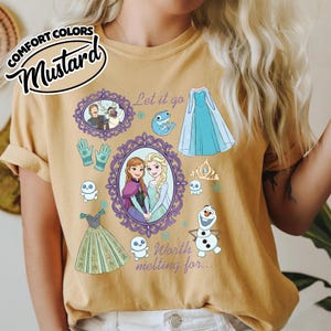 Op de afbeelding: Mosterdkleurig T-shirt met illustraties van personages en elementen uit de animatiefilm. Het ontwerp bevat ingelijste portretten, een blauwe jurk, handschoenen, een kroon en de tekst "Let it go" en "Worth melting for..."