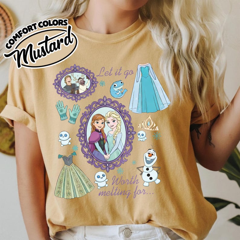 Op de afbeelding: Mosterdkleurig T-shirt met illustraties van personages en elementen uit de animatiefilm. Het ontwerp bevat ingelijste portretten, een blauwe jurk, handschoenen, een kroon en de tekst "Let it go" en "Worth melting for..."