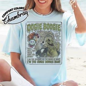 May include: Light blue t-shirt with a graphic featuring the text "Oogie Boogie" and illustrations of characters from a movie. The shirt also has the text "I'm the Oogie Boogie Man!"