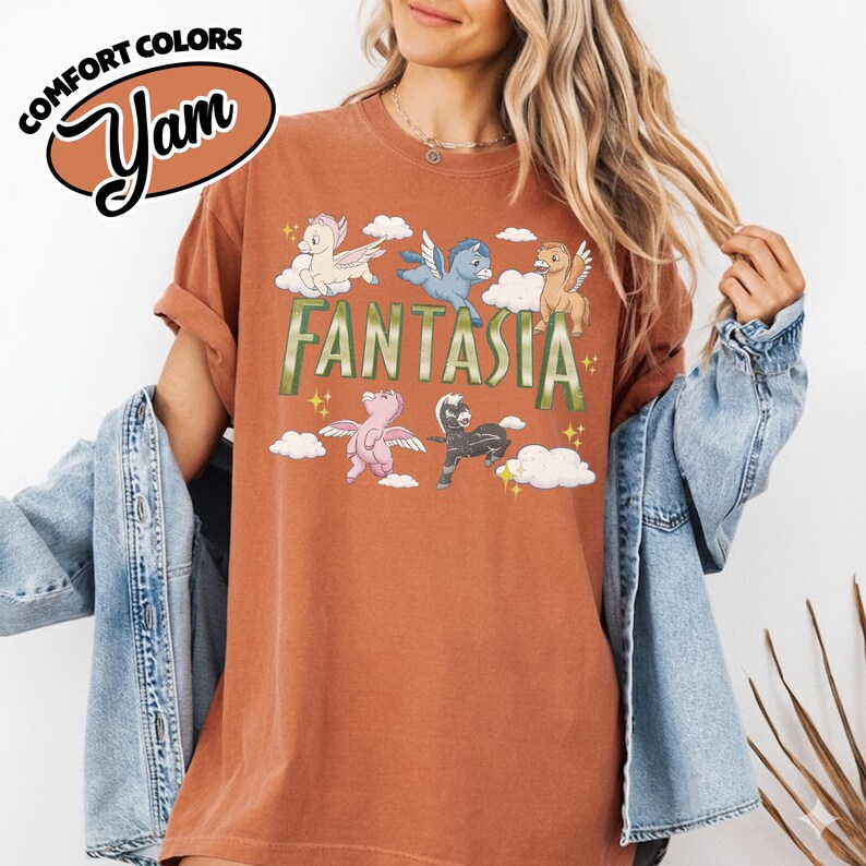 May include: A rust-coloured t-shirt with the word "Fantasia" in green letters and cartoon pegasus characters. The shirt has the words "Comfort Colors" and "Yam" in a brown oval.