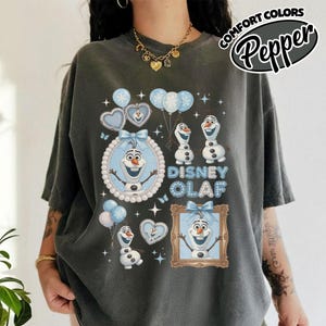 May include: Dark gray t-shirt featuring a Disney Olaf design. The design includes images of Olaf, balloons, hearts, and the text "Disney Olaf." The shirt also has the text "Comfort Colors Pepper" in a circular design.