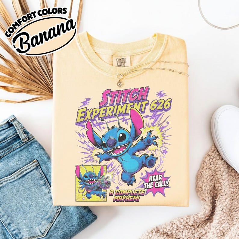 Może przedstawiać: Bladoż&oacute;łty t-shirt z grafiką przedstawiającą niebieską postać Stitcha z Eksperymentu 626. Wz&oacute;r zawiera fioletowe błyskawice, mniejszy panel w stylu komiksowym ze Stitchem oraz tekst Stitch Experiment 626, Hear the Call i A Complete Mayhem.