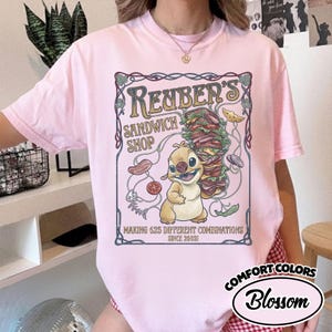 K&ouml;nnte beinhalten: Hellrosa T-Shirt mit einem Cartoon-Motiv f&uuml;r "Reuber's Sandwich Shop". Das Design zeigt ein Sandwich, eine Zeichentrickfigur und den Text "Making 625 Different Combinations Since 2003!". Das Shirt hat auch das "Comfort Colors"-Logo.