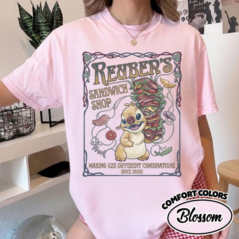 K&ouml;nnte beinhalten: Hellrosa T-Shirt mit einem Cartoon-Motiv f&uuml;r "Reuber's Sandwich Shop". Das Design zeigt ein Sandwich, eine Zeichentrickfigur und den Text "Making 625 Different Combinations Since 2003!". Das Shirt hat auch das "Comfort Colors"-Logo.