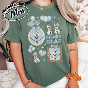May include: Moss green t-shirt featuring the text "Disney Olaf" with images of Olaf the snowman, balloons, and hearts. The shirt has a round neck and short sleeves. The Comfort Colors logo is in the upper left corner.
