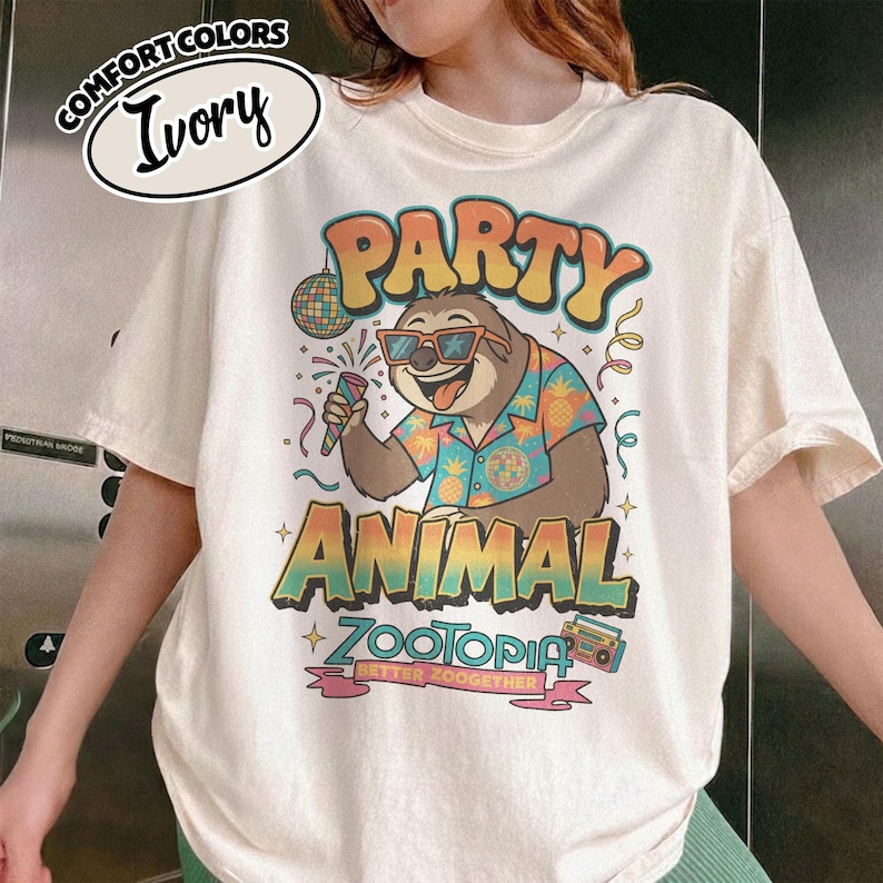 Puede incluir: Camiseta de color marfil con un gr&aacute;fico de un perezoso con gafas de sol y una camisa hawaiana, sosteniendo un micr&oacute;fono. La camiseta presenta las palabras "PARTY ANIMAL ZOOTOPIA BETTER ZOOGETHER" en colores vibrantes, con una bola de discoteca y un radiocasete.