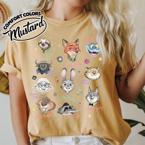 K&ouml;nnte beinhalten: Senffarbenes T-Shirt mit Illustrationen von Zeichentrickfiguren. Das Shirt enth&auml;lt den Text "COMFORT COLORS" und "Mustard" in einer stilisierten Schriftart. Das Shirt zeigt verschiedene Gesichter von Charakteren aus einem beliebten Animationsfilm.