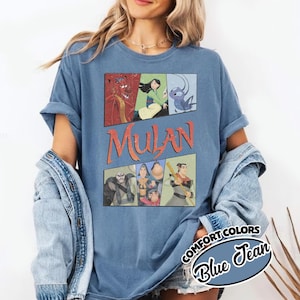 Puede incluir: Camiseta azul Comfort Colors con un gr&aacute;fico de personajes de Mulan en paneles de estilo c&oacute;mic. La palabra "Mulan" est&aacute; en letras naranjas. La camiseta tambi&eacute;n tiene una etiqueta "Blue Jean".