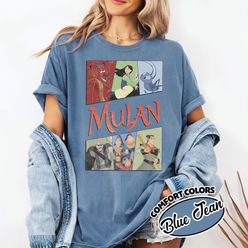 Puede incluir: Camiseta azul Comfort Colors con un gr&aacute;fico de personajes de Mulan en paneles de estilo c&oacute;mic. La palabra "Mulan" est&aacute; en letras naranjas. La camiseta tambi&eacute;n tiene una etiqueta "Blue Jean".